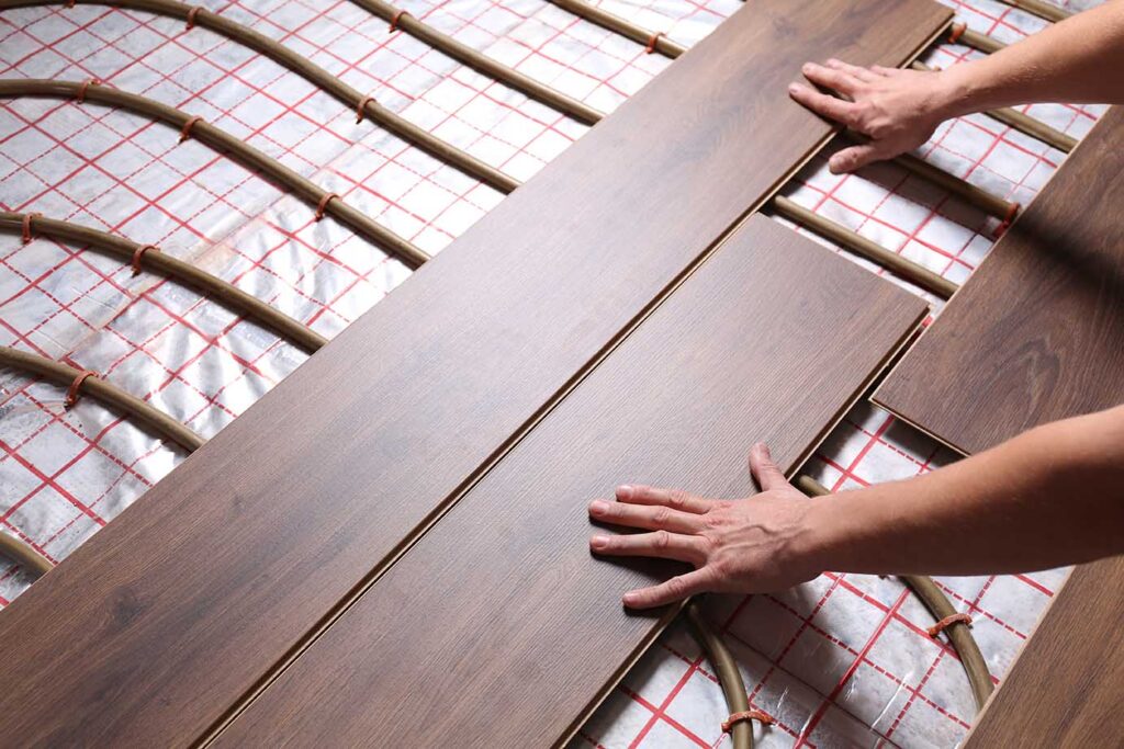 Worker installing new wooden laminate over underfloor heating system